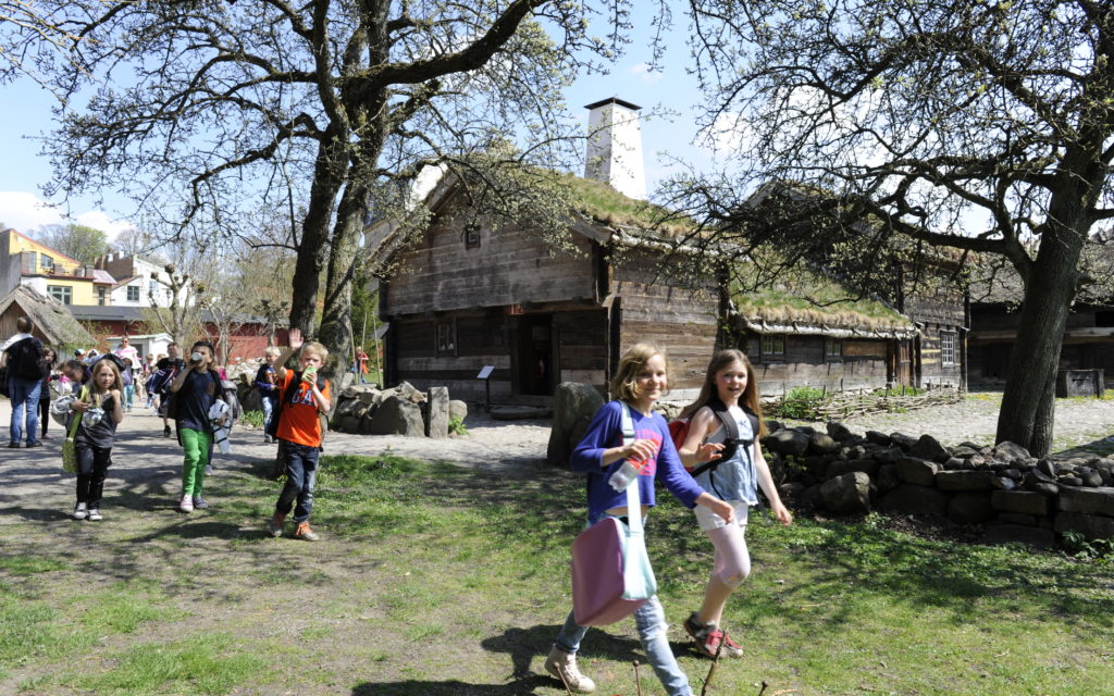 Skolbarn i friluftsmuseet med Blekingegården i bakgrunden. En vårdag.