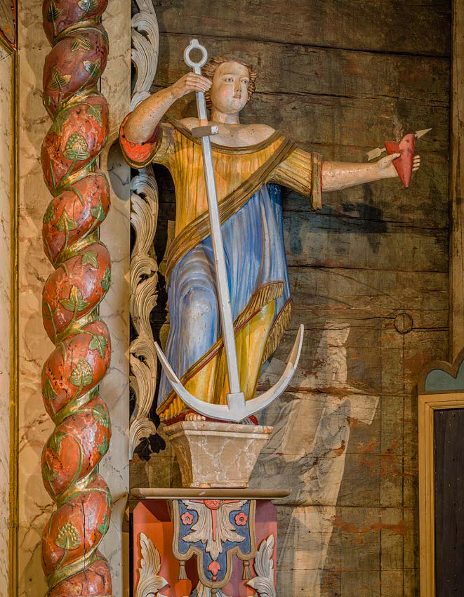 Detalj från altartavlan. En symbolisk figur som med den ena handen håller om ankaret som är hoppets tecken. I den andra handen håller hon det brinnande hjärtat, sinnebilden för Jesus kärlek. 
