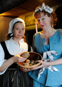 Pedagoger klädda som piga respektive prästfru under 1700-talet. Pigan har en skål med potatis i famnen.