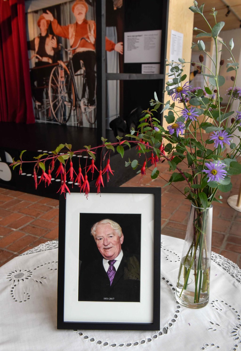 Porträtt av Hasse Alfredson bredvid en vas med blommor i utställningen Hasse och Tage