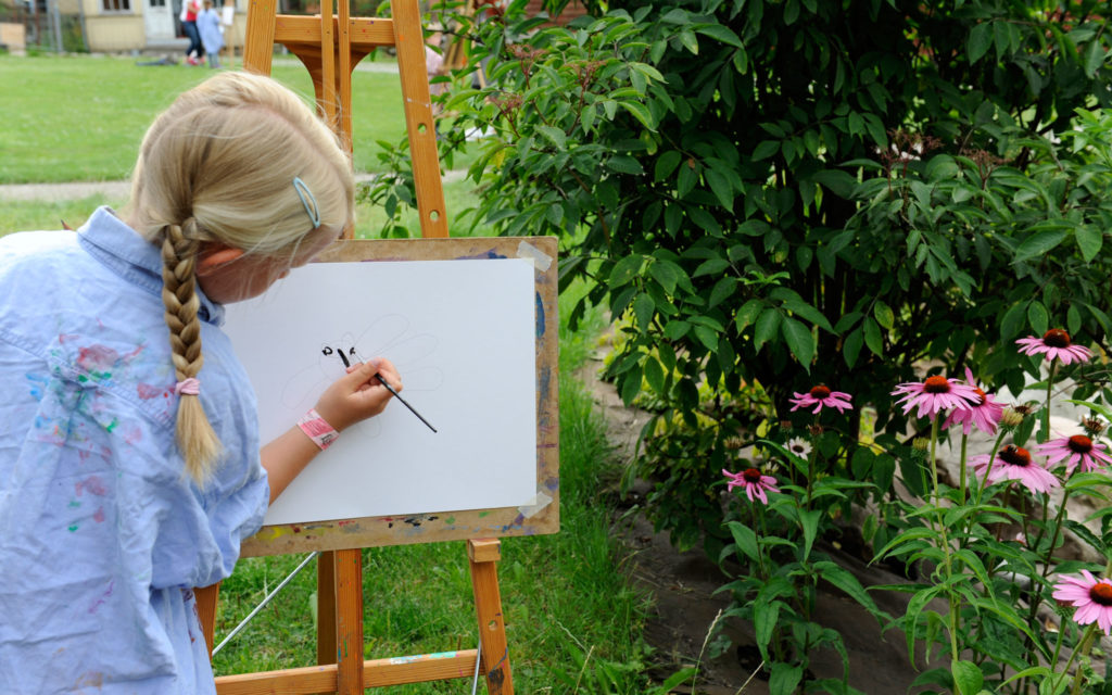 Flicka målar tavla i trädgården på museet