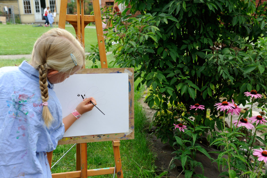 Flicka målar tavla i trädgården på museet