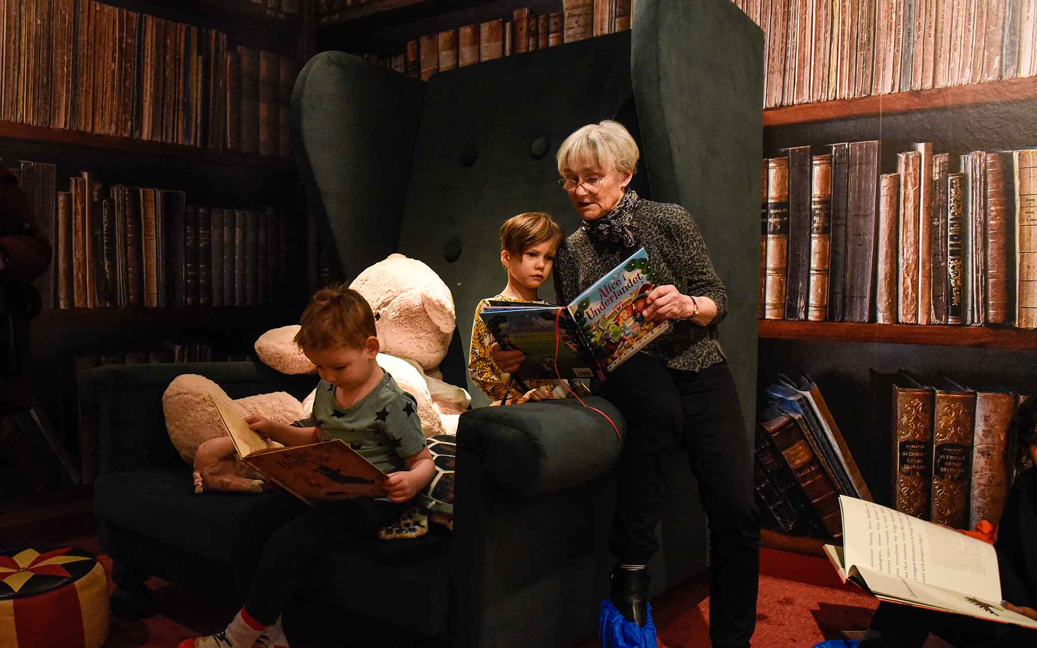 Två barn och en vuxen läser böcker i en jättestor fåtölj