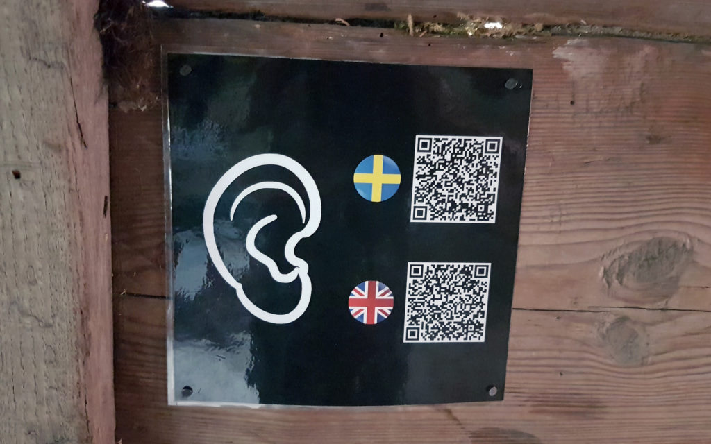 Skylt på väggen, med ett öra och QR-koder. 