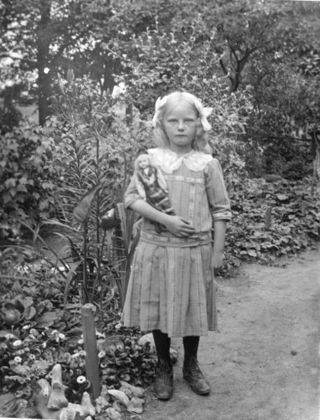 Flicka som håller en docka i famnen. Finklädd med rosetter i håret. Foto: Otto Hoffer, ur Kulturens samlingar