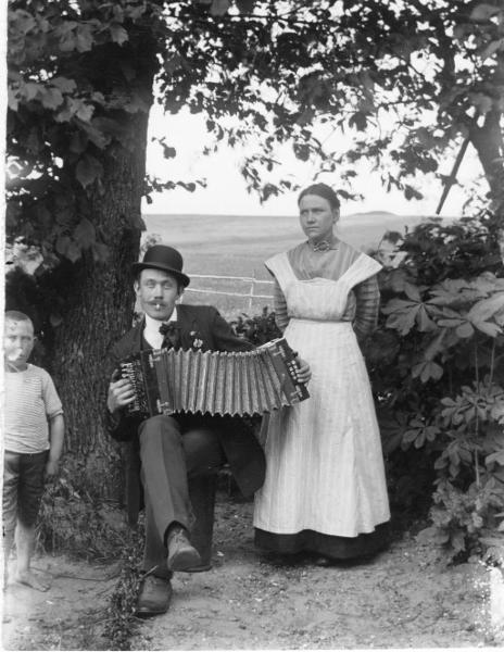  Målare Frans Persson sitter och spelar dragspel, till vänster står hans hustru Emma och till höger en pojke, kanske deras son? Foto: Otto Hoffer, ur Kulturens samlingar. 