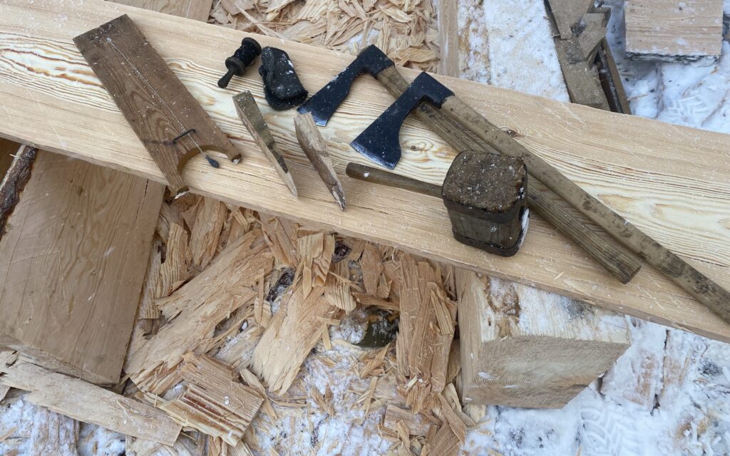 På en träbräda ligger två yxor, en träklubba och några andra verktyg som användes under arbetet med att klyva en stock till brädor.